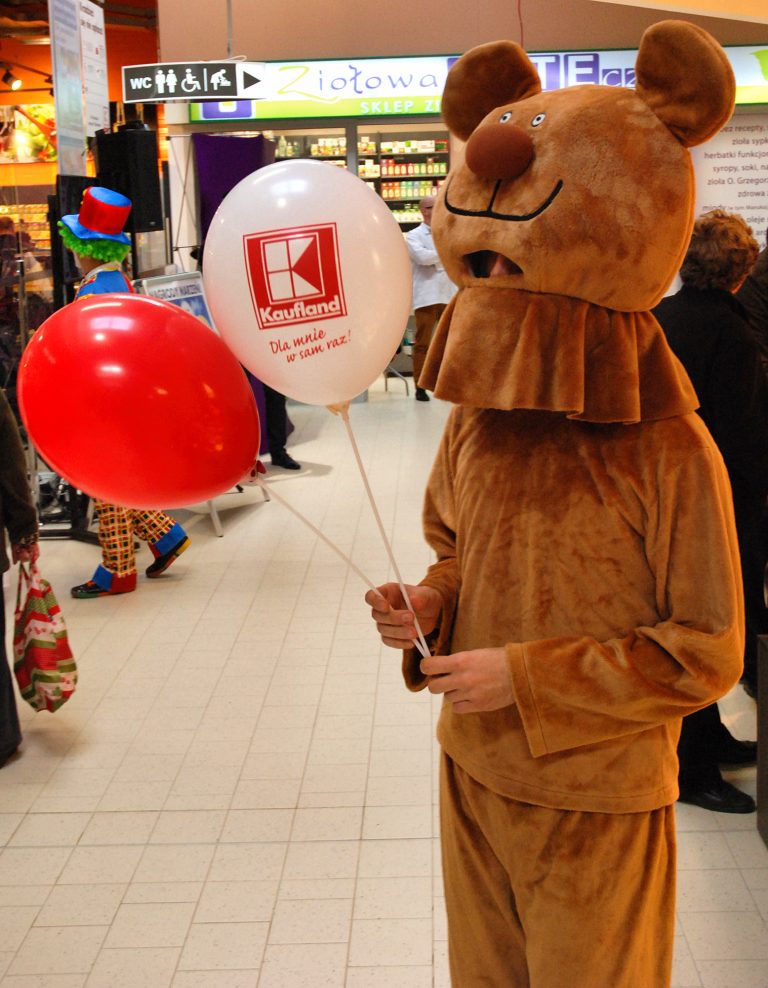 Maskotka rozdaje balony reklamowe na patyczkach